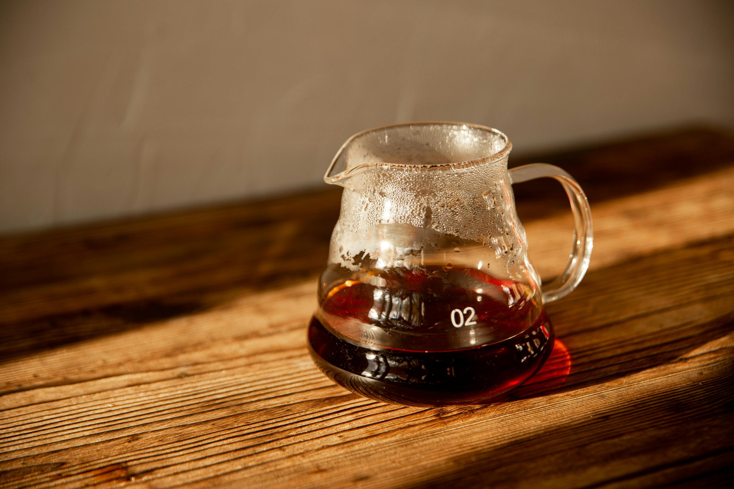 A close-up of freshly brewed coffee in a glass carafe with steam, set on a rustic wooden table.