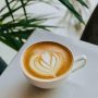 A beautifully crafted latte art in a white coffee cup with a leaf design on a table.