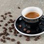 Stylish espresso served in a black cup on a saucer with scattered coffee beans.